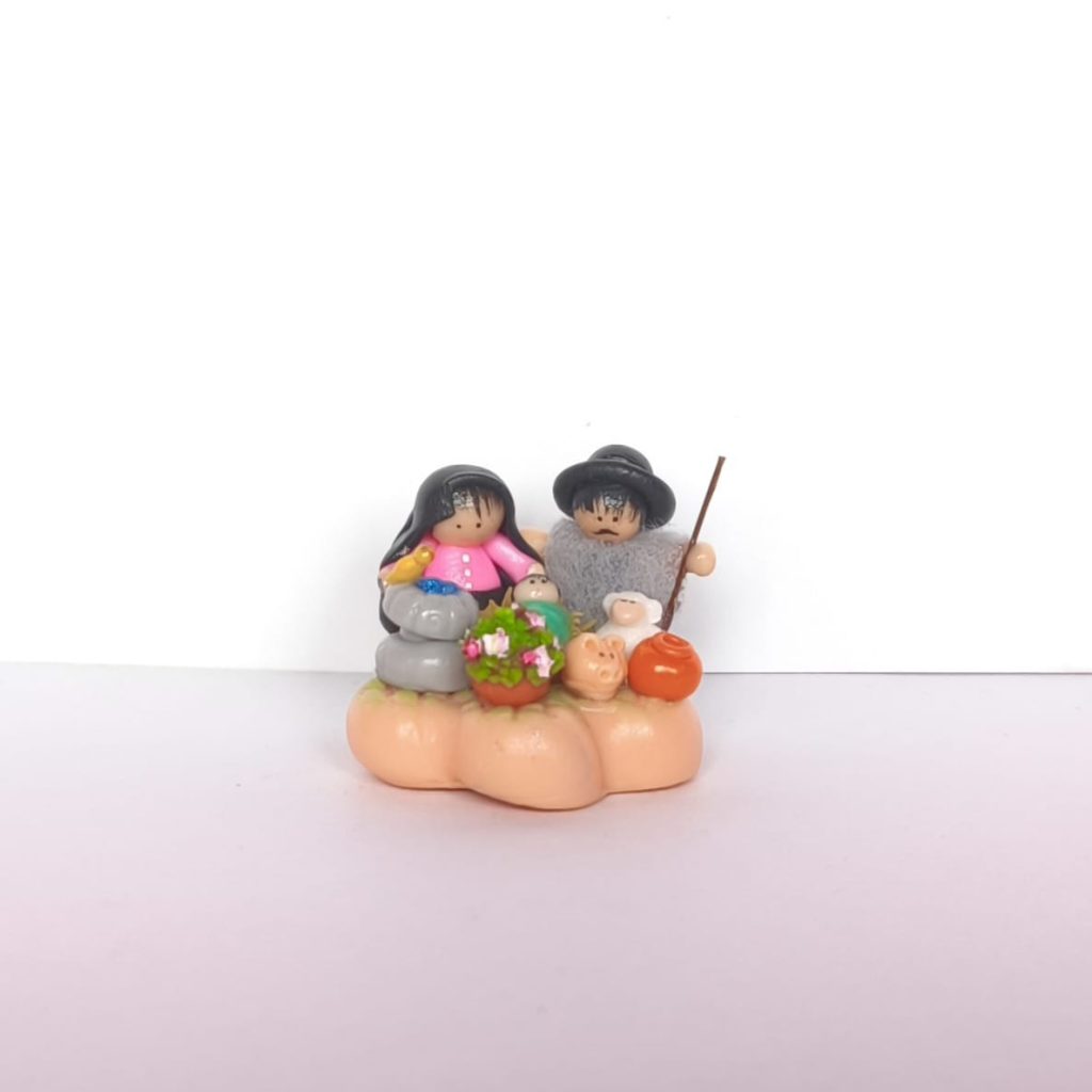 Pesebre artesanal con figuras campesinas, animales y flores sobre base decorativa.