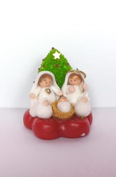 Pesebre en miniatura artesanal con la Sagrada Familia vestida de blanco frente a un árbol de Navidad verde con estrella dorada, sobre base roja.