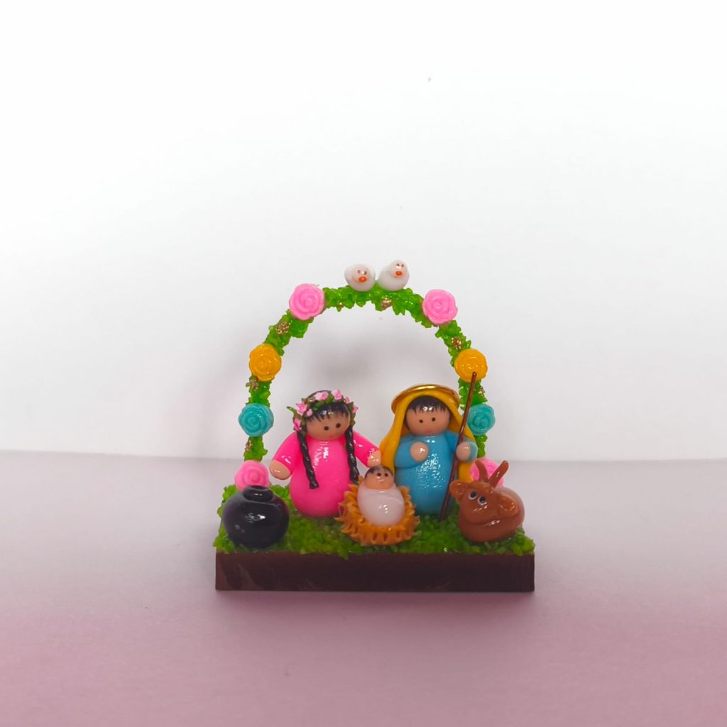 pesebre en miniatura que muestra la Sagrada Familia rodeada con arco de flores y dos palomas sobre base de madera.