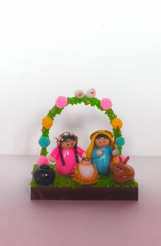 pesebre en miniatura que muestra la Sagrada Familia rodeada con arco de flores y dos palomas sobre base de madera.