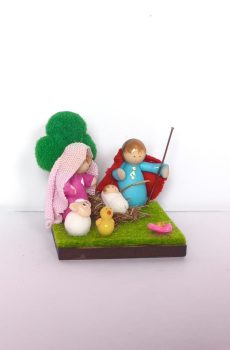 Pesebre en miniatura artesanal con la Sagrada Familia con mantas en tela, sobre base verde con flor y pollito.